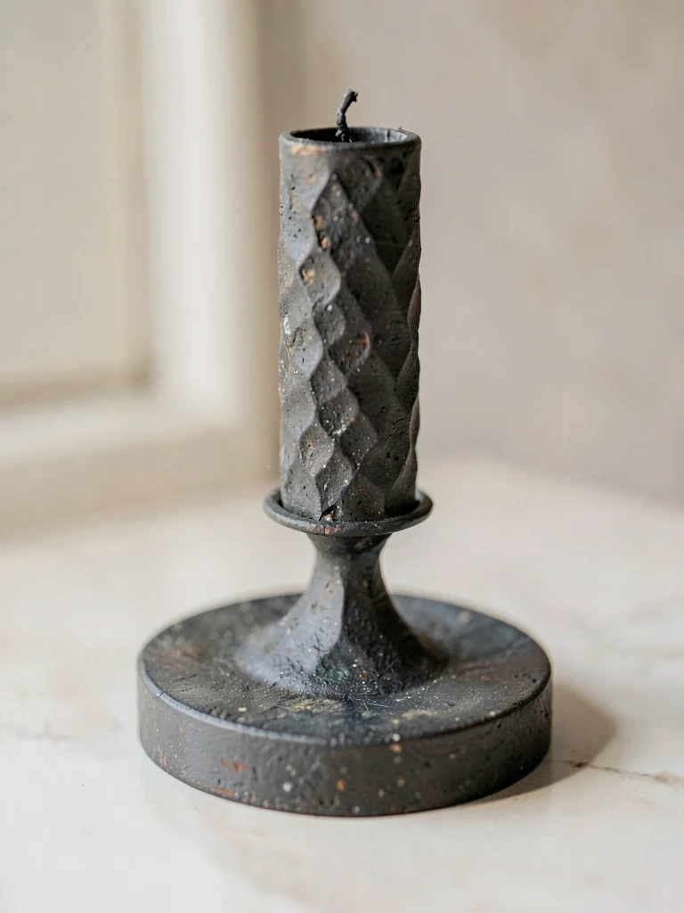 The hand-forged iron candlestick rests heavy showing rough hammered facets and a