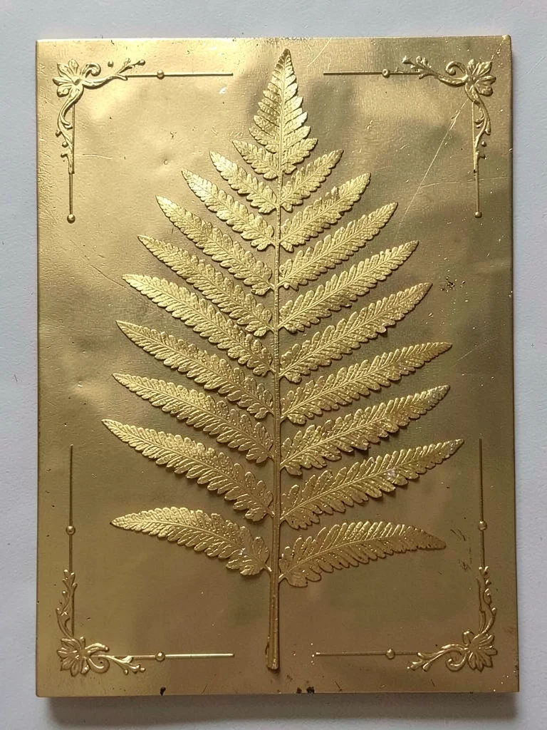 A fern frond pressed flat, gold covering the central vein and leaflet tips