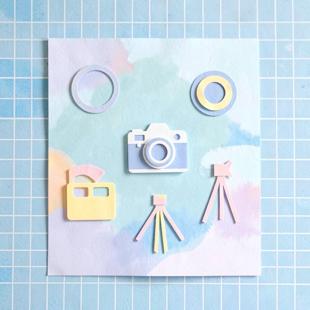 Bright cut-paper layout of camera icons (lens, flash, tripod, film) on a sky-blu