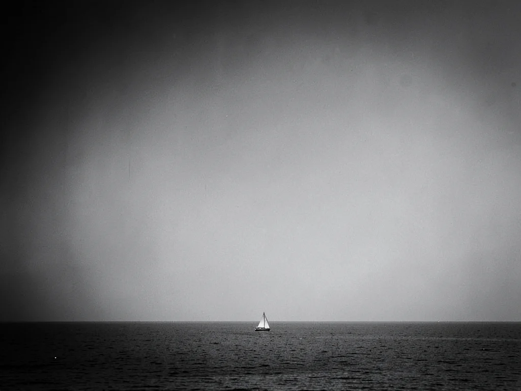 Tiny sailboat in lower third surrounded by monochrome sea and sky