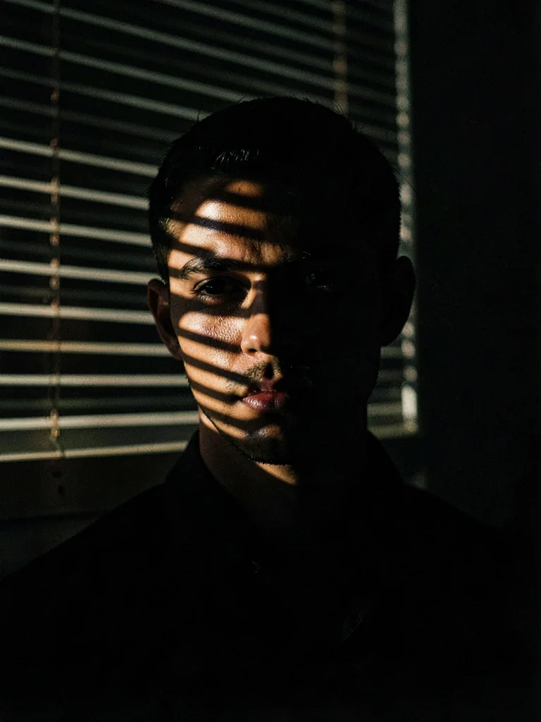 Silhouette at venetian blinds, stripes of light cutting horizontal across face a