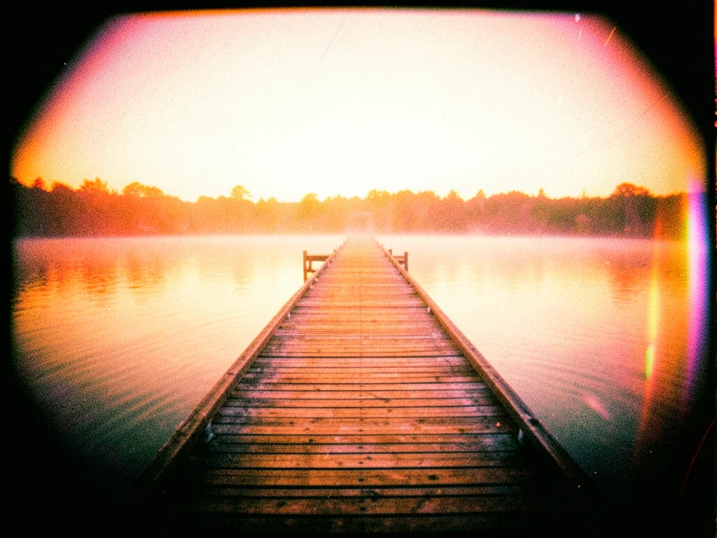 A pier stretching into a lake at dawn, the wood and water in warm amber tones, m