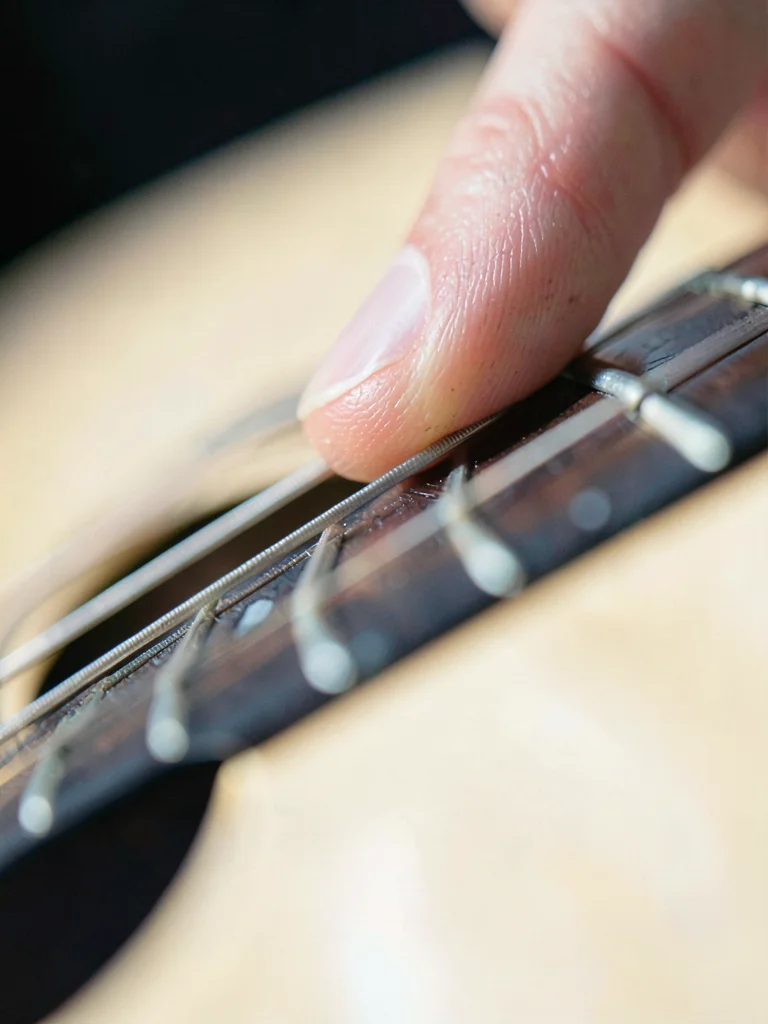 Guitarist's fingertip pressing fret, string indentation visible, neck of guitar 