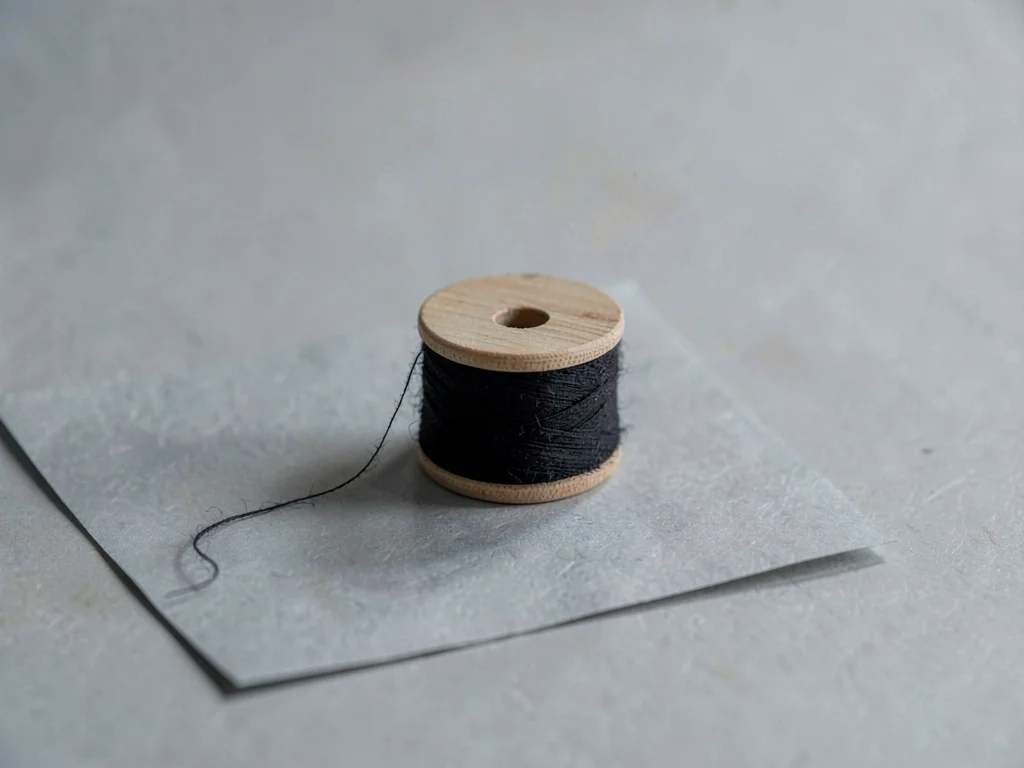 One black-stained wooden spool of unbleached cotton thread resting on cool-grey 