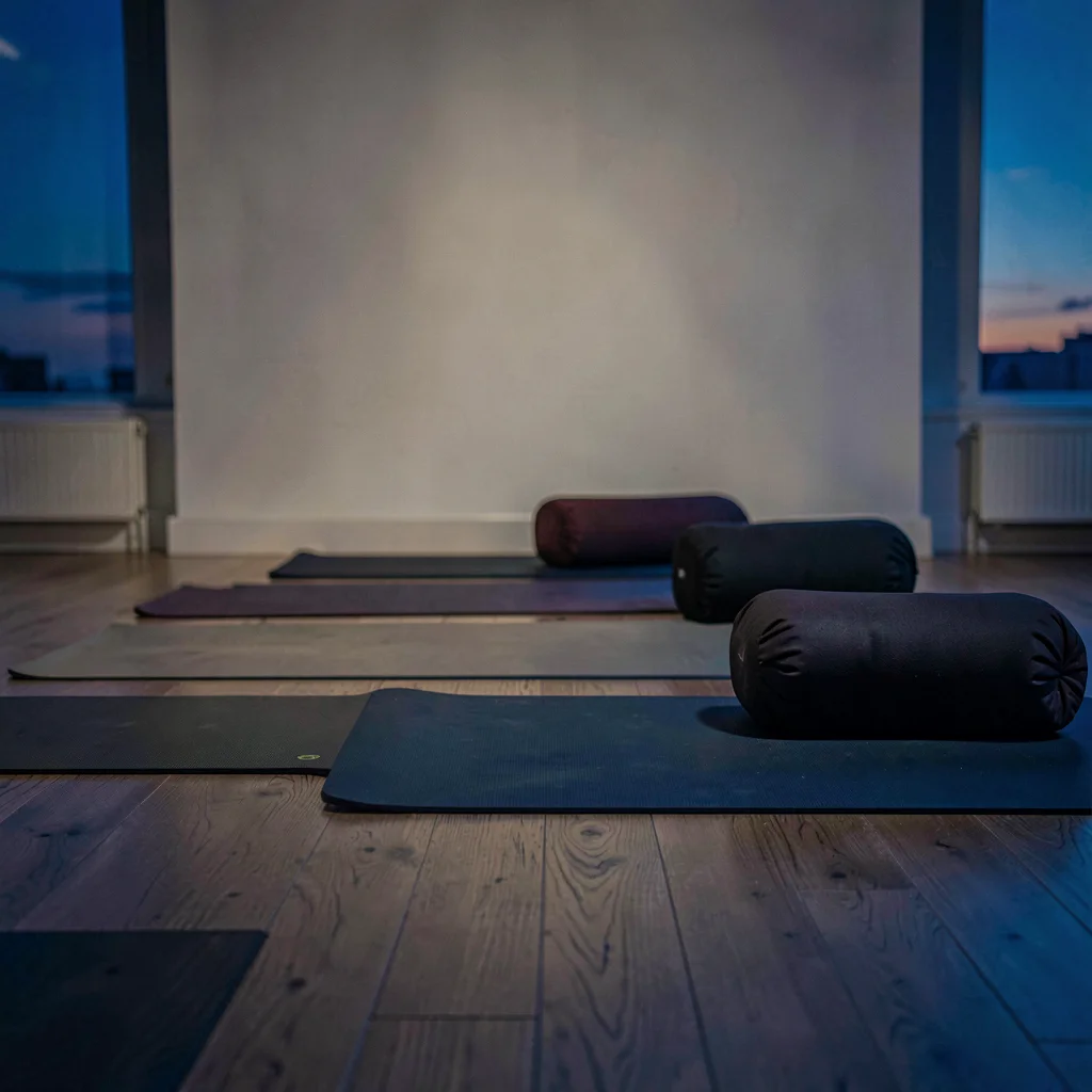 Quiet studio scene at twilight, a row of mats and bolsters on a wooden floor, de