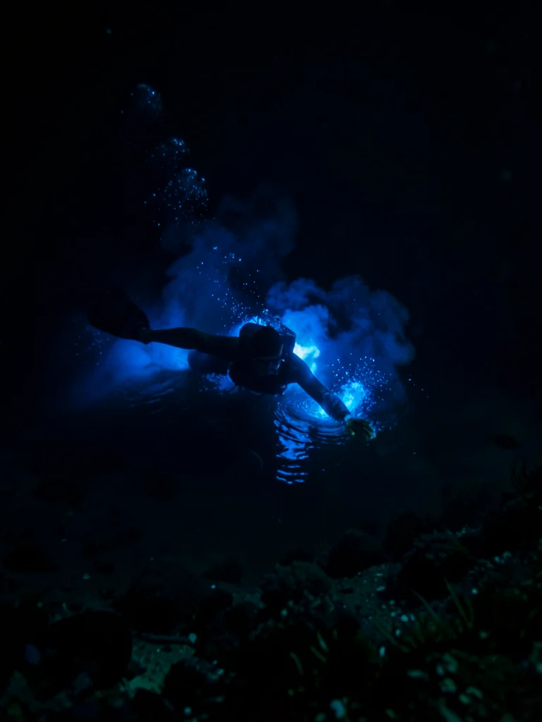 Night swimmer surrounded by blue glow — figure in dark water with luminous blue 