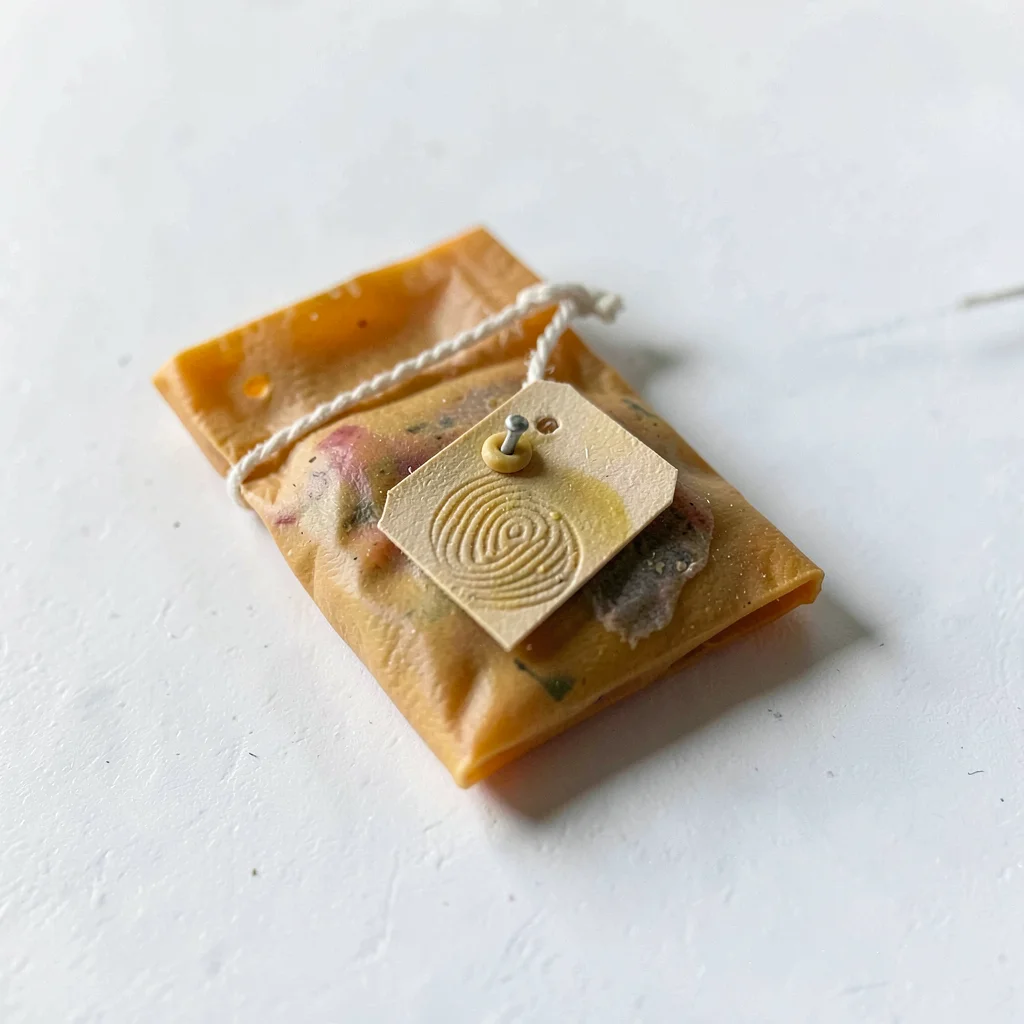 Dampened ochre tea bag with a slumped tag and fingernail-pressed staple, on plai