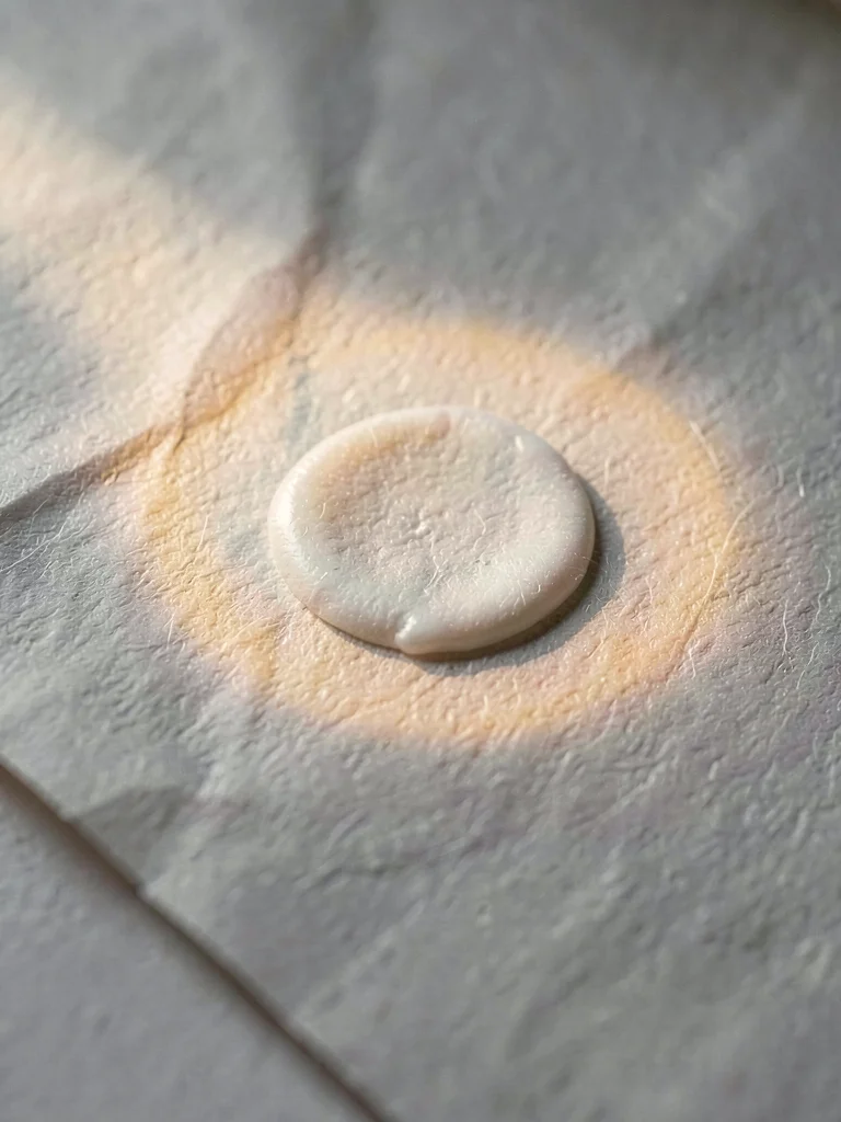 Glue-spot raised mound on parchment catching directional light with warm fiber h