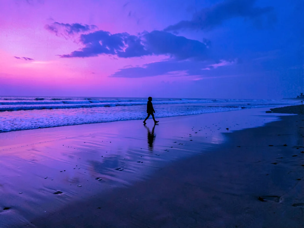 Solitary figure walking tide line at blue hour, wet sand reflecting impossible p