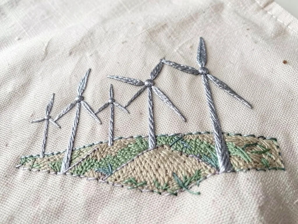A row of wind turbines on a hillside, their blades in silver metallic thread