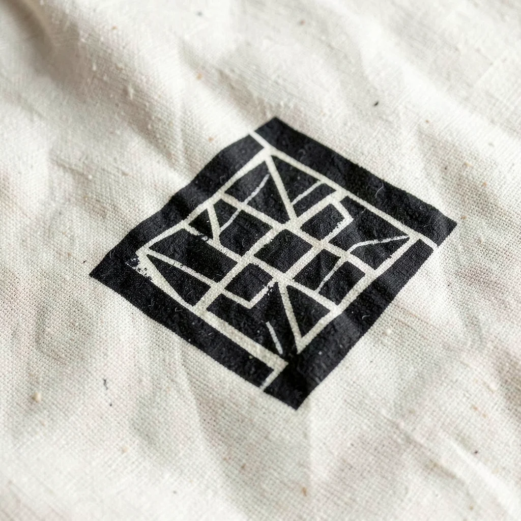 Single Sankofa symbol macro on natural cotton — strong geometric form, black on 