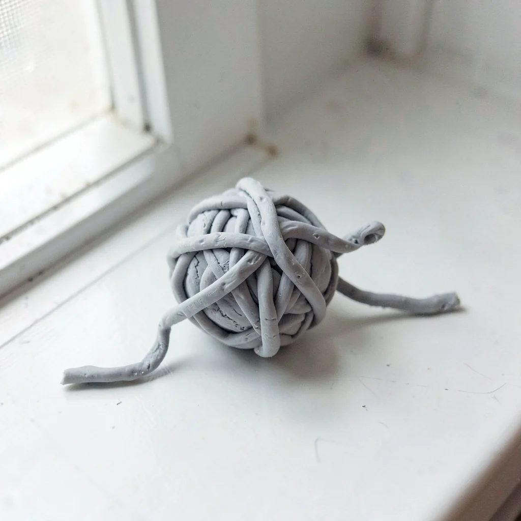 Twined putty-grey ball of string with thumb dents at the loose tail and fingerna