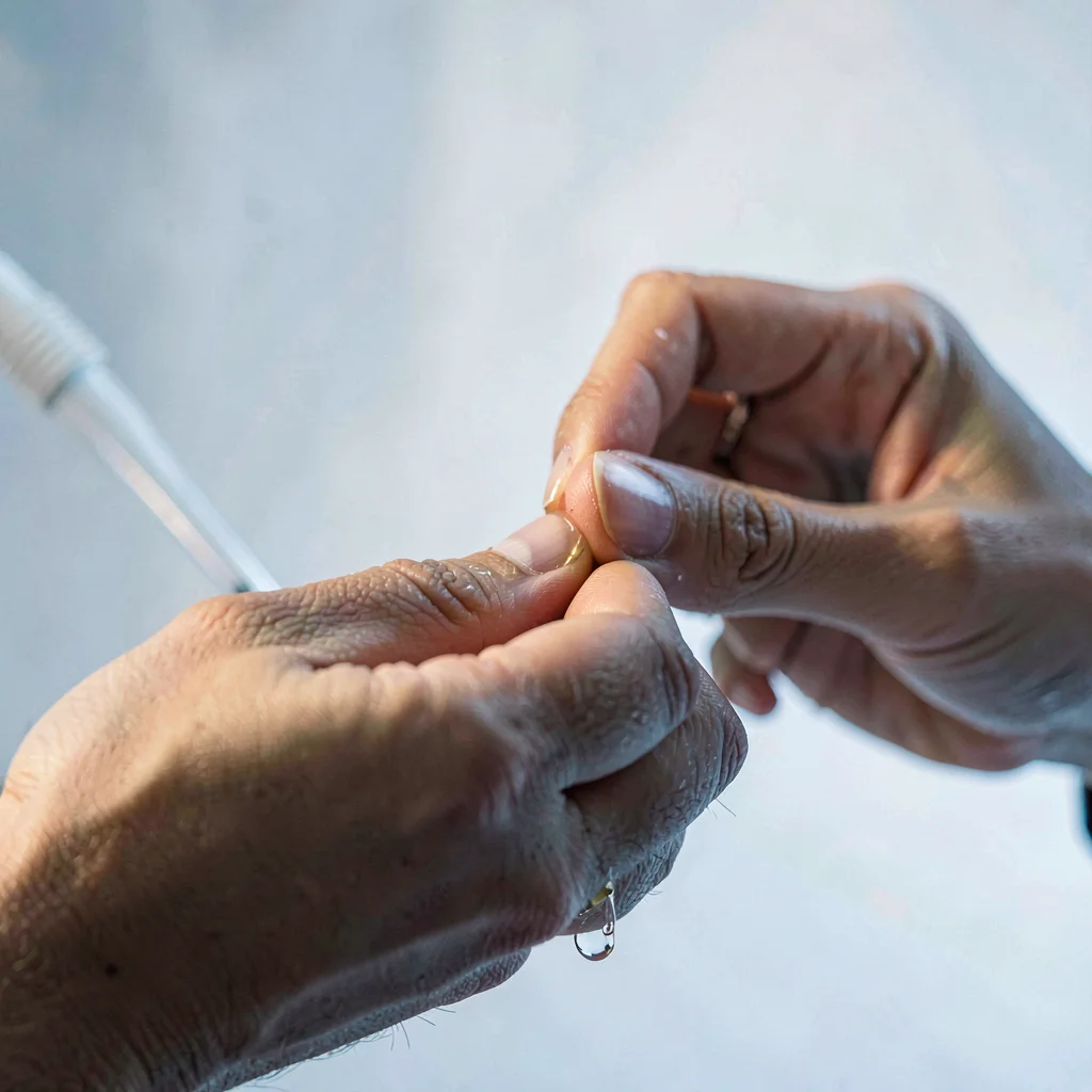 Editorial close-up of a model's hands rubbing oil between fingertips, soft cool 
