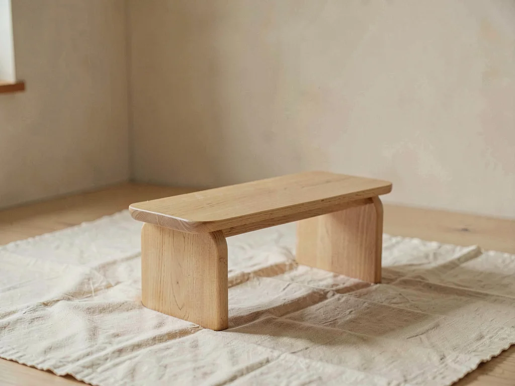One small low wooden bench of pale oak with rounded apron centered on cream line