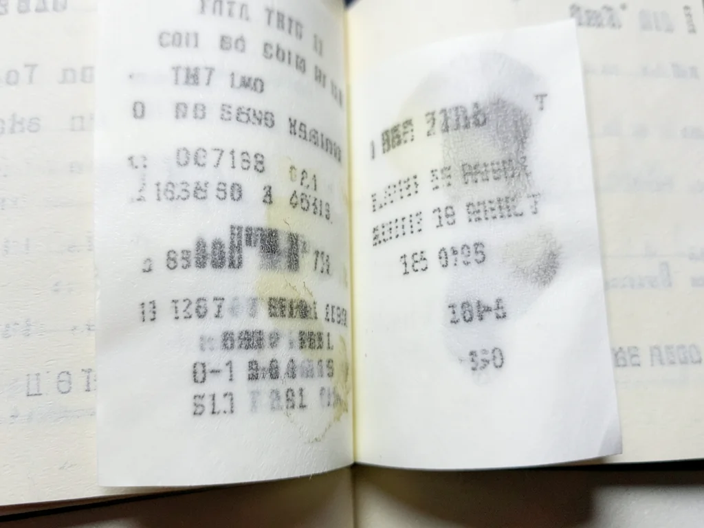 Thermal receipt pressed between book pages for years, text transferred ghostly o