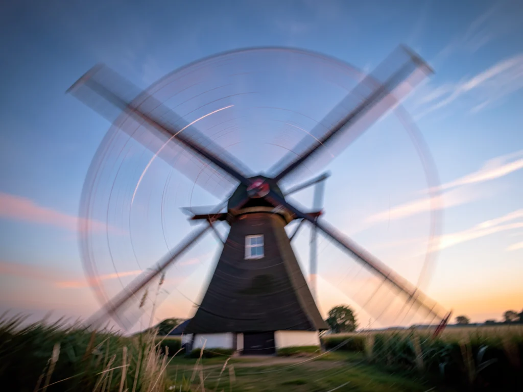 Windmill blades blurred into translucent circular disc against Dutch sky