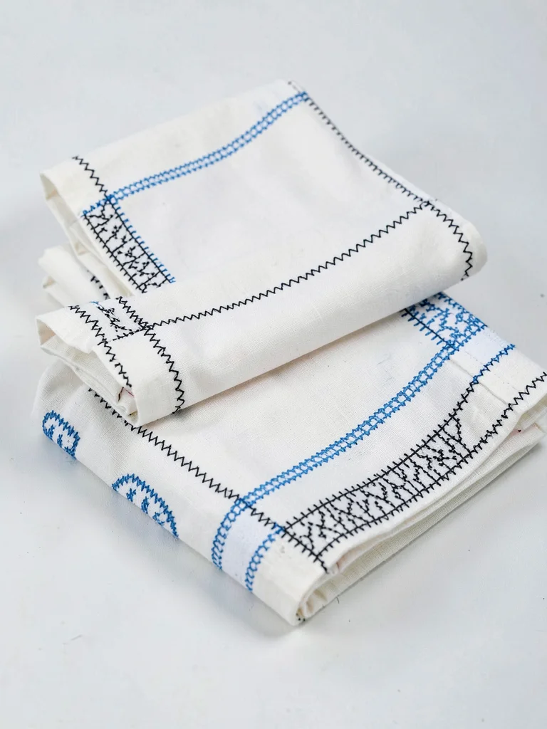 Folded Ainu garment stack — three robes folded with embroidery borders visible a