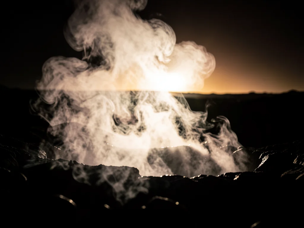 Volcanic fumarole with sulfurous steam, backlit by setting sun, raw geological p