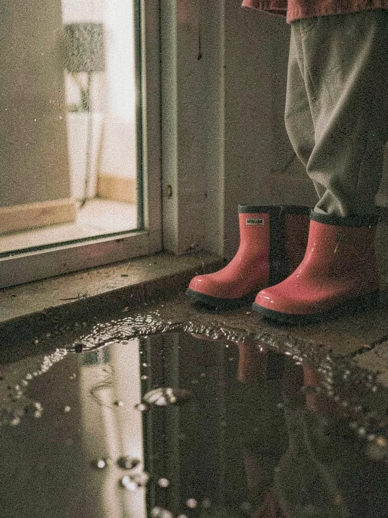 Child's rain boots left by a screen door, puddle reflecting bare bulb light, hea