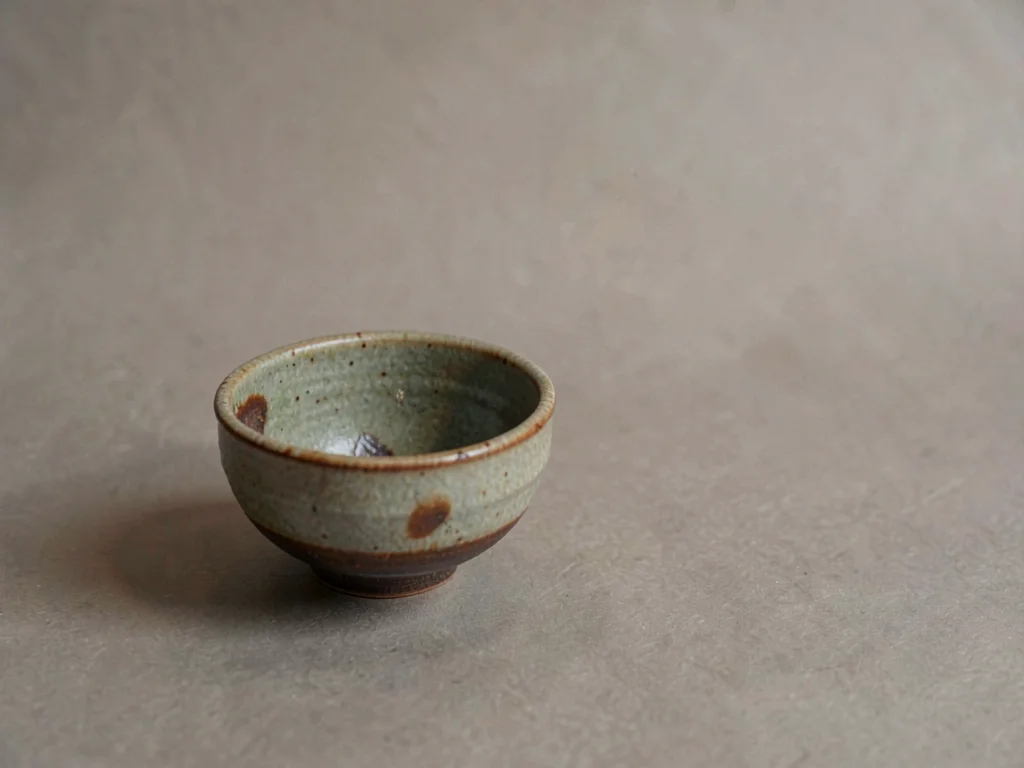 A small Bizen-ware bowl placed low-left on warm-grey paper, kiln-flashed surface