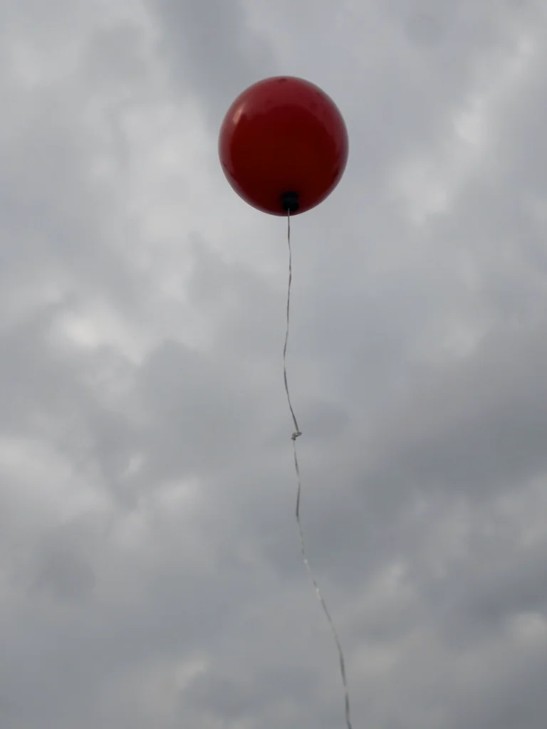 Child's balloon escaping into gray sky, the string still visible, the letting go