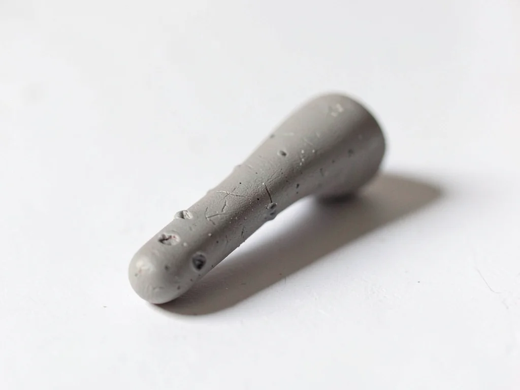 Burnished putty-grey shoe horn with a slumped curve and fingernail dents along i