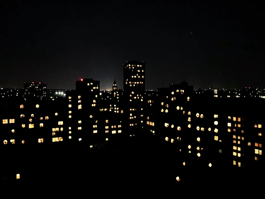 Cityscape at night but all lights are holes poked in black paper, light behind
