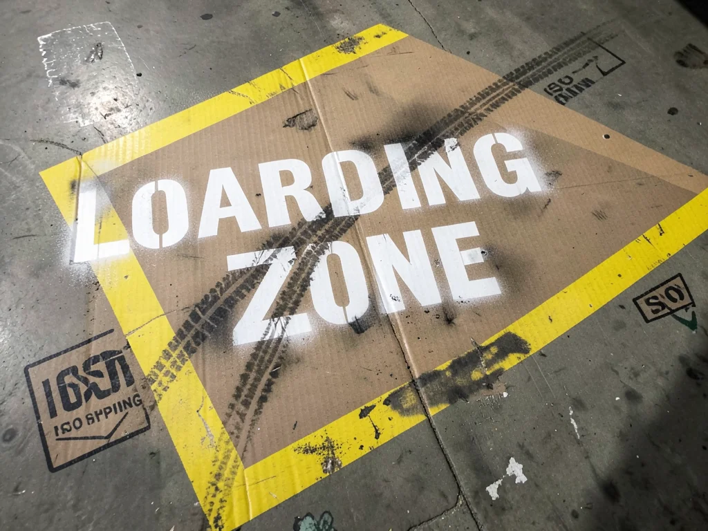 A warehouse floor with painted zone markings — yellow diagonal hazard stripes, l