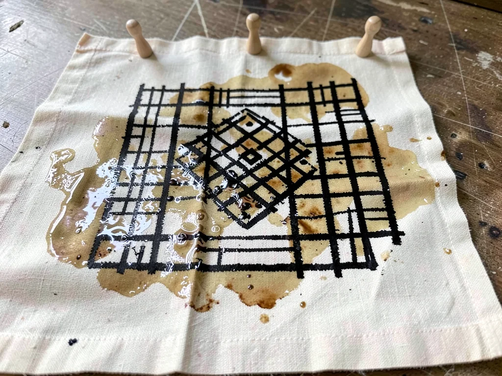 Freshly stamped cloth drying — cloth pegged flat, dye still wet and gleaming