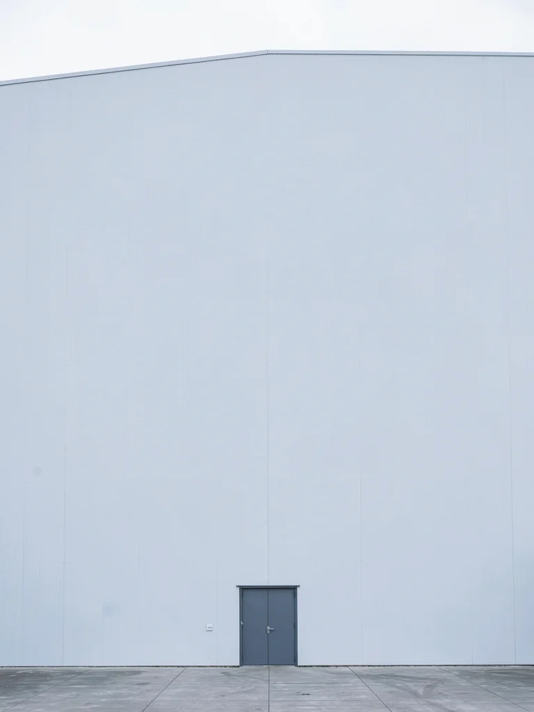 Single door at bottom of towering white warehouse wall
