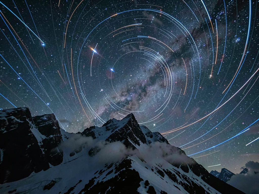 Night sky with star trails circling around Polaris over mountain peak