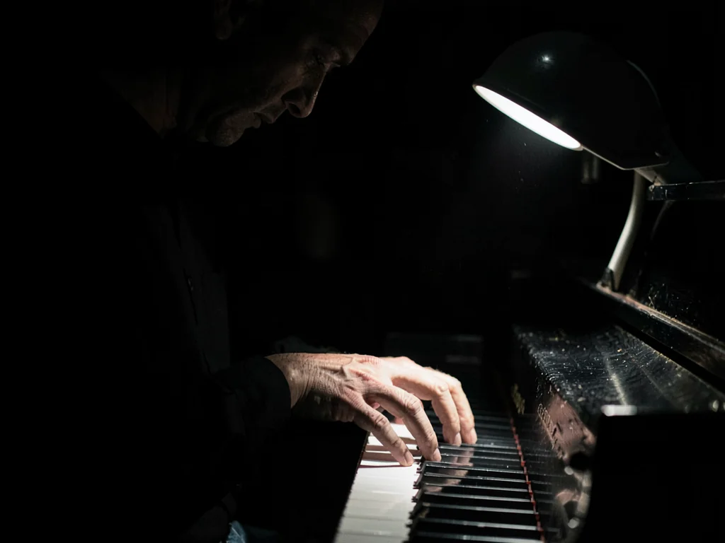 Pianist hands on keys, practical lamp on piano the only light, keys alternating 