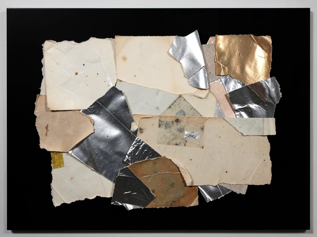 Torn metallic wrapping paper fragments on matte black, reflective scraps catchin