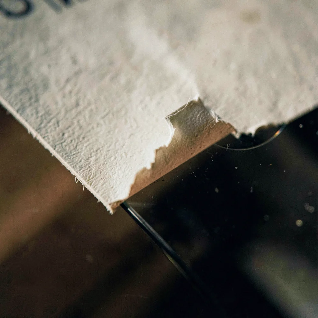 Tight texture study of a hand-pressed paper label peeling at the corner against 