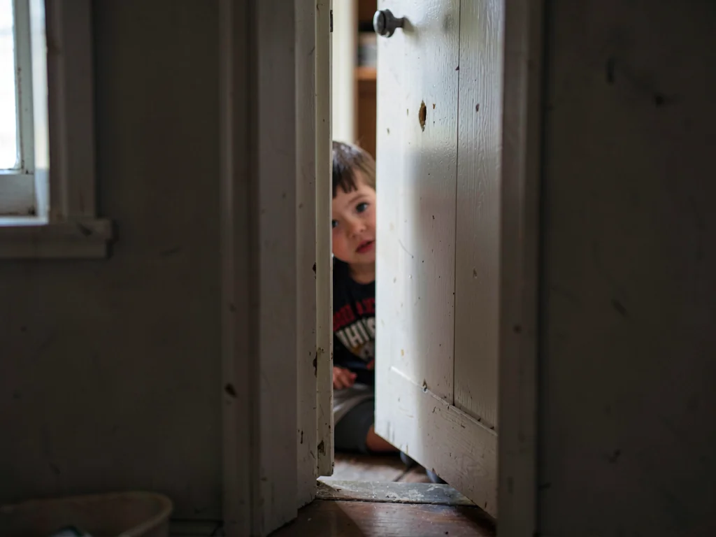 Child hiding behind half-open closet door, eye visible in the crack, the doorway