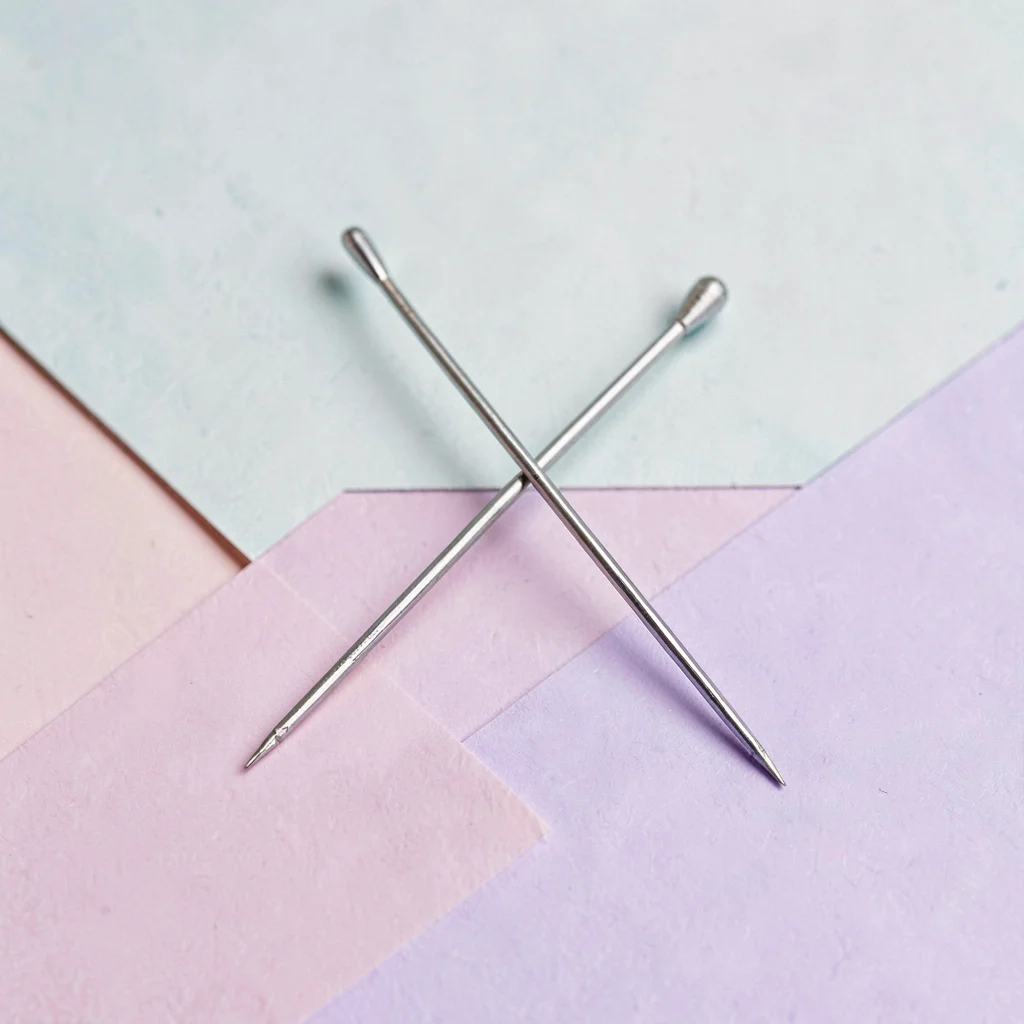 Two needle pairs crossed in an X on a flat color block