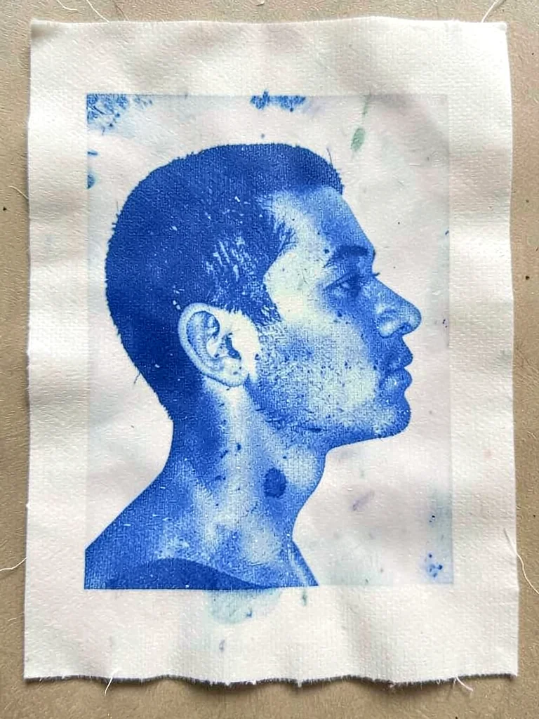 A face pressed in profile onto sensitized paper — blue silhouette, fabric grain 