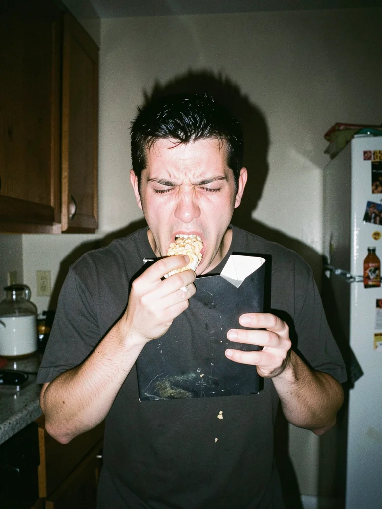 Person eating cereal directly from box while crying, standing in kitchen at 2am,