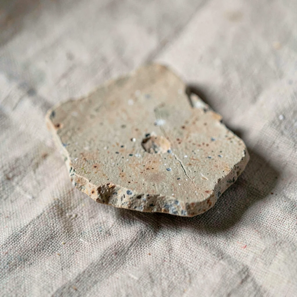 macro of a chipped pottery shard on neutral linen, mineral-cut detail