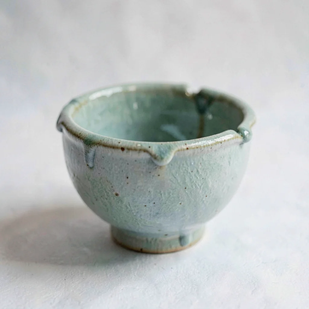 A small ceramic ash glaze cup rests showing dripping tonal celadon glaze and an 