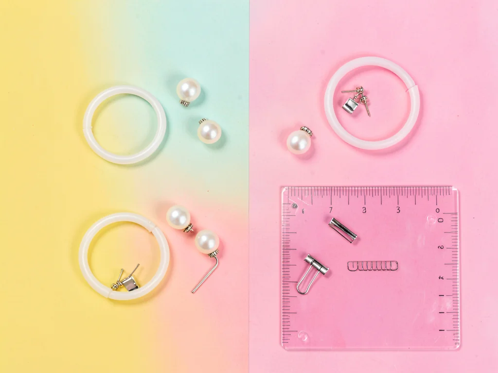 Bird's-eye flat-lay of pearl earrings, plastic bangles, hair clips, and a transl
